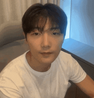 a man in a white t-shirt is sitting on a couch and looking at the camera .