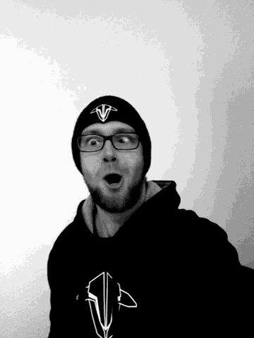 a man wearing glasses and a beanie with the letter v on it looks surprised