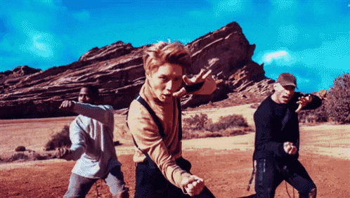 a group of young men are dancing in a field with a mountain in the background