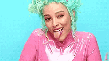 a woman with green hair is sticking her tongue out and wearing a pink outfit .
