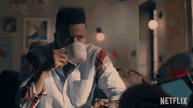 a man sitting on a couch drinking a cup of coffee with netflix in the background