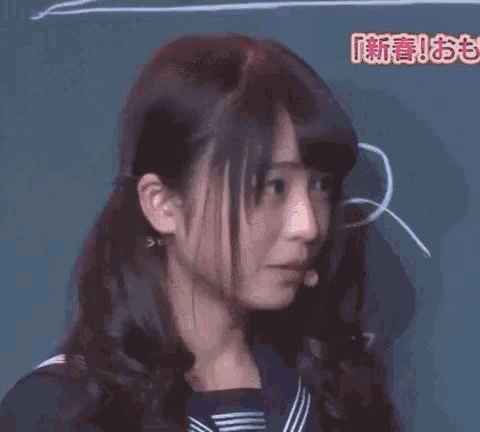 a young woman in a school uniform is standing in front of a blackboard with chinese writing on it .