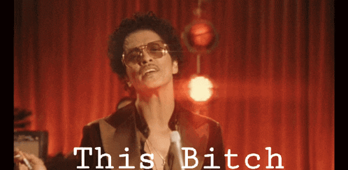 a man in a suit and sunglasses stands in front of a red curtain with the words " this bitch " on it