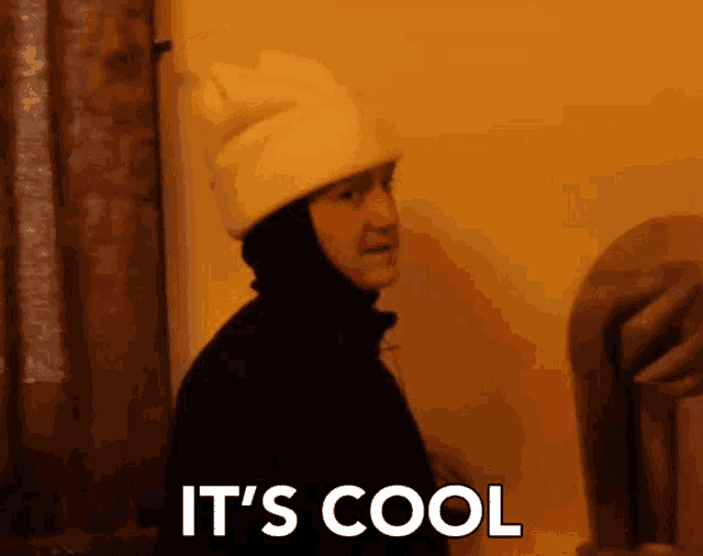 a person wearing a white hat and a black jacket with the words it 's cool written on it