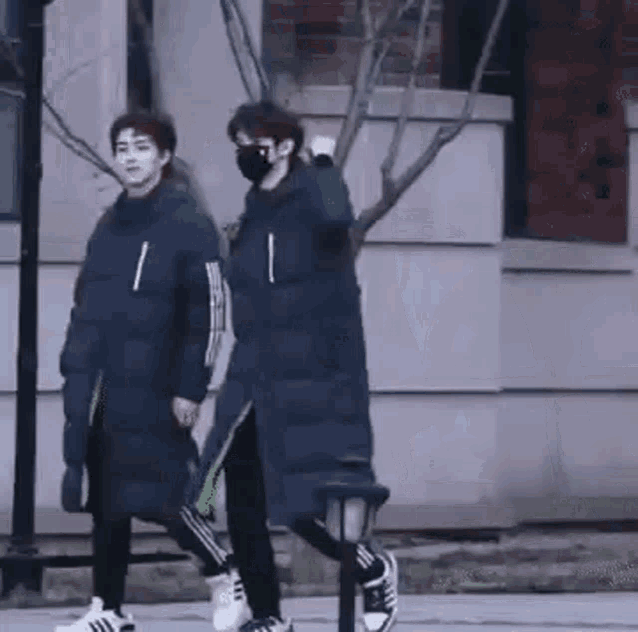 two people wearing masks are walking down the street .