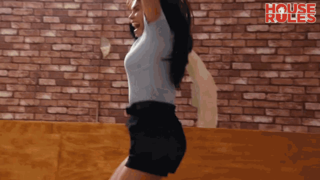 a woman is dancing in front of a brick wall with the words house rules written on it