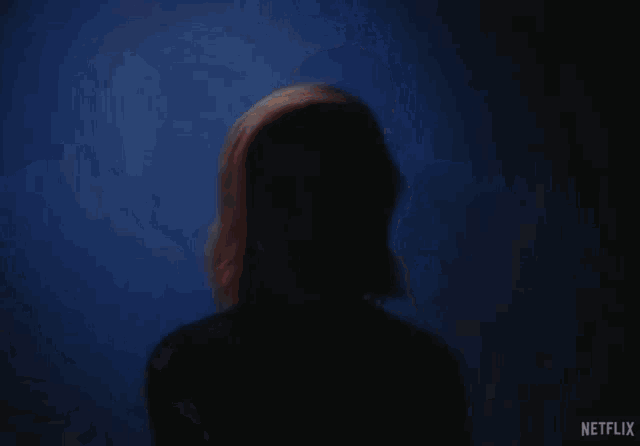 a man and a woman are standing in a dark room and the woman is wearing a black sweater with the word netflix on it