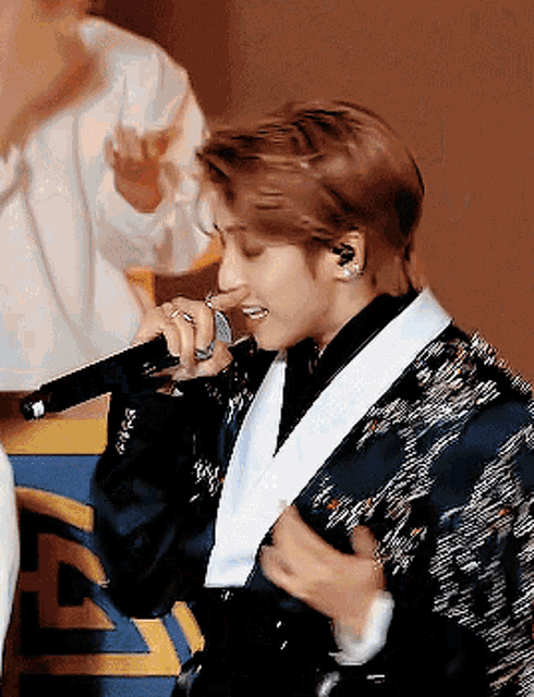 a man in a suit is singing into a microphone while wearing earrings