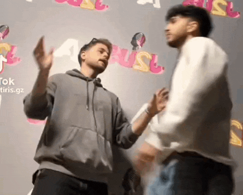 two men are standing next to each other in front of a wall and dancing .