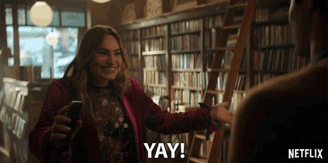 a netflix ad shows a woman in a library holding a phone and saying yay