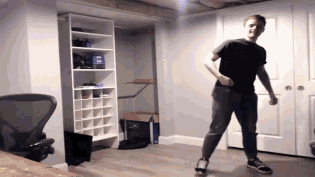 a man in a black shirt is dancing in a room with a chair
