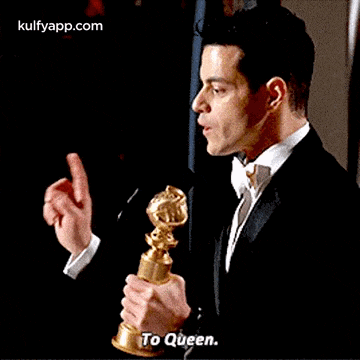 a man in a tuxedo is holding a golden globes trophy and says `` to queen '' .