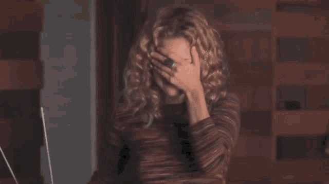 a woman with curly hair is covering her face with her hand while sitting in front of a laptop computer .