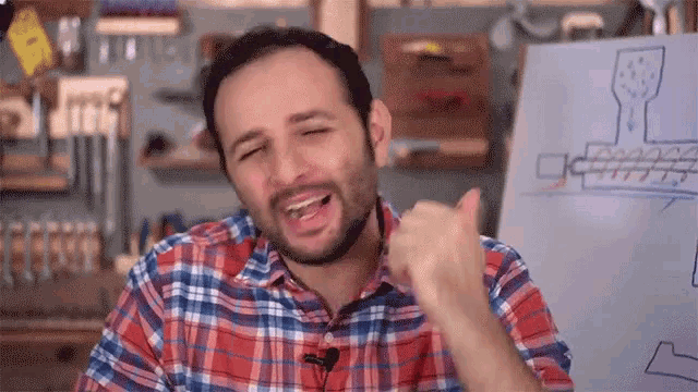 a man in a plaid shirt is giving a thumbs up in front of a white board