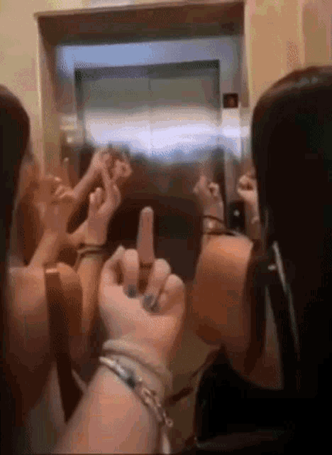 a group of people are sitting in an elevator making a heart shape with their hands .