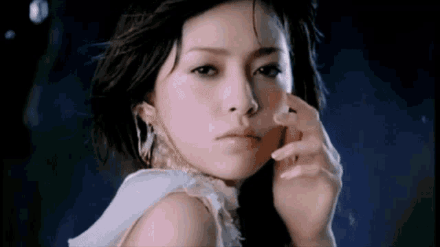 a woman in a white dress looks at the camera with her hand on her face