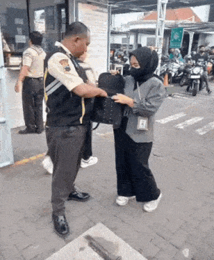 a woman in a hijab is holding a black bag and talking to a man in a uniform .