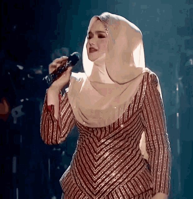 a woman singing into a microphone wearing a hijab