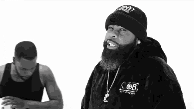 a man with a beard wears a black beanie and a black coat with the word ob on it