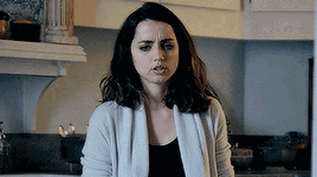 a woman is standing in a kitchen wearing a white cardigan and a black top .