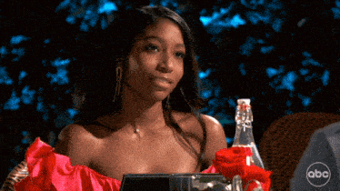 a woman in a red dress sits at a table with a bottle of abc water
