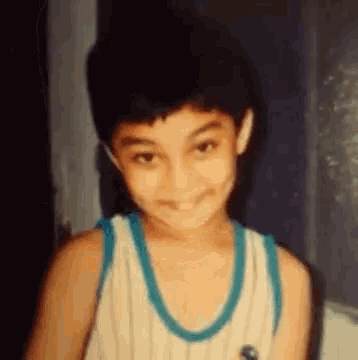 a young boy wearing a striped tank top and a blue necklace is smiling .
