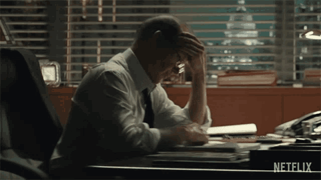 a man in a suit and tie is sitting at a desk with his head in his hands .