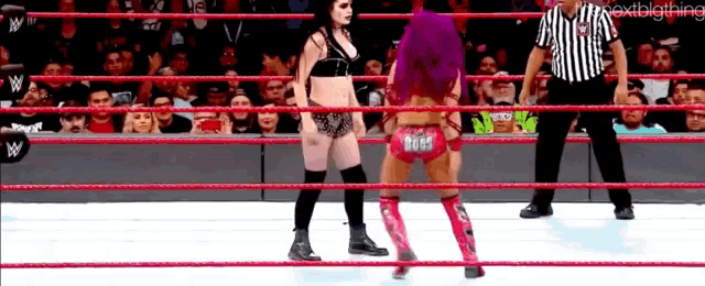 two women are wrestling in a wrestling ring while a referee stands behind them .