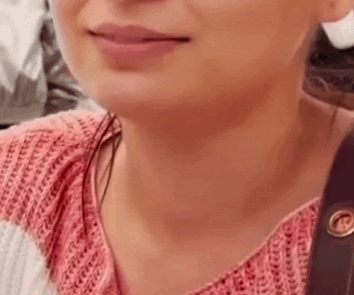 a close up of a woman 's face with a pink sweater on .