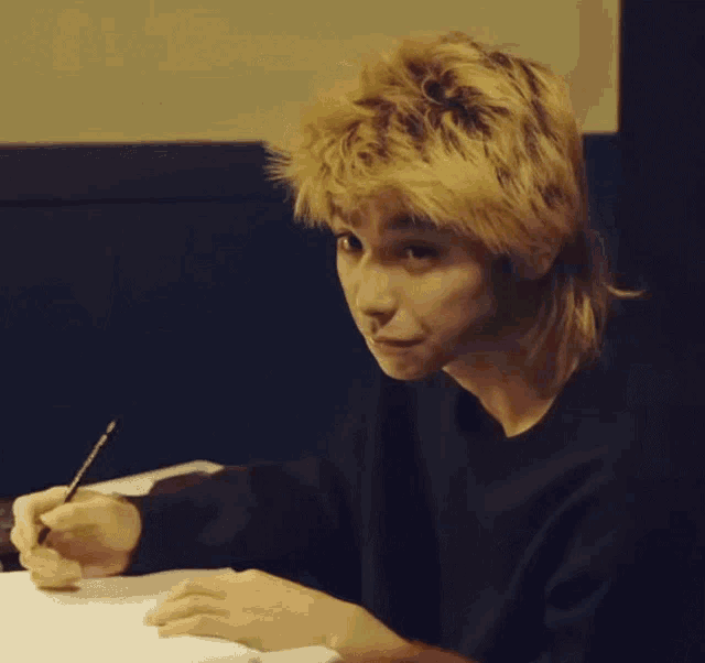 a woman with blonde hair is writing on a piece of paper with a pen