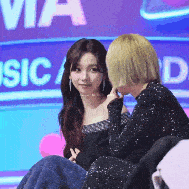 two women are sitting next to each other on a stage in front of a sign that says music awards .