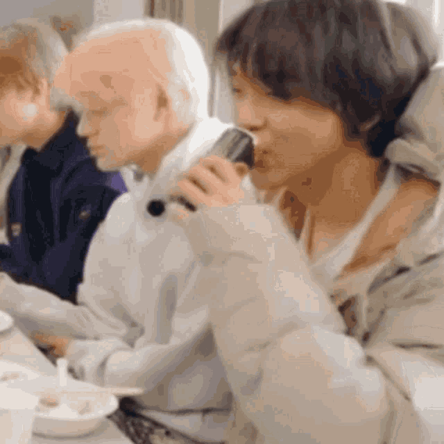 a group of people are sitting at a table drinking from a bottle