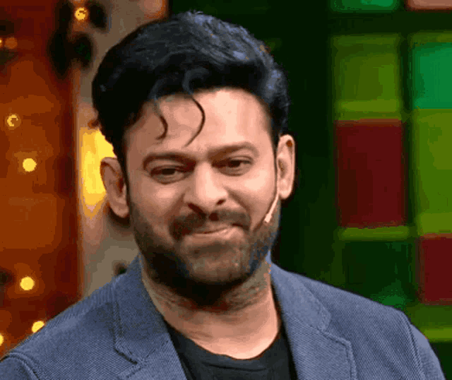 a man with a beard is wearing a blue jacket and black shirt and making a funny face .