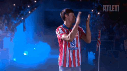a man in a red and white striped shirt applauds in front of an athlete logo
