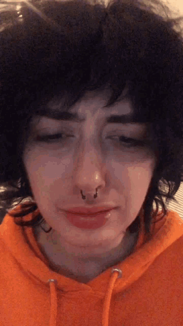 a woman with a nose ring and an orange hoodie looks sad