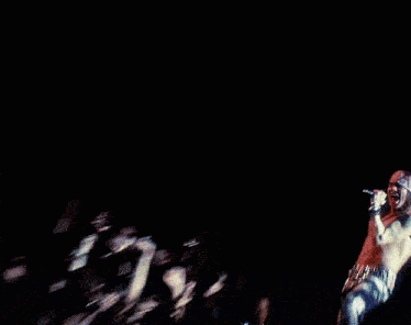 a shirtless man with a bandana on his head sings into a microphone