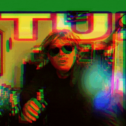 a man wearing sunglasses is holding a bottle of beer in front of a sign that says tu