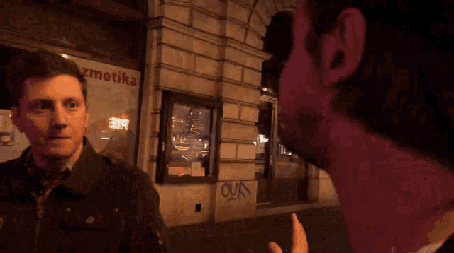 a man talks to another man in front of a store that says kozmetika