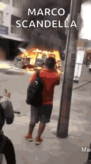 a man is taking a picture of a car on fire with the words marco scandella written above him .