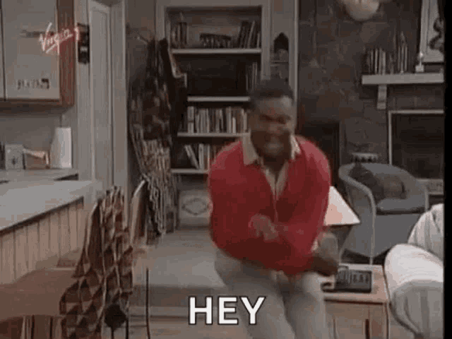 a man in a red sweater is dancing in a living room with the words `` hey '' .