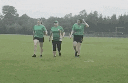 three women are walking on a field wearing green shirts and shorts .
