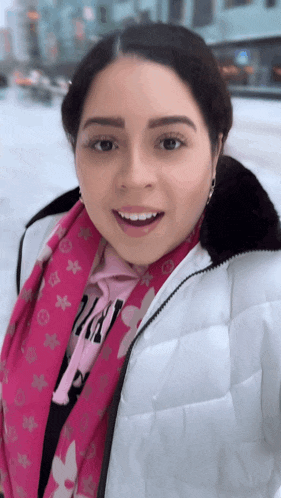 a woman wearing a pink louis vuitton scarf and a white jacket smiles for the camera