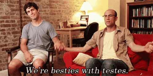 two men are sitting on a red couch holding hands with the words we 're besties with testes written above them