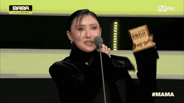 a woman is holding a trophy and speaking into a microphone at a mama awards ceremony