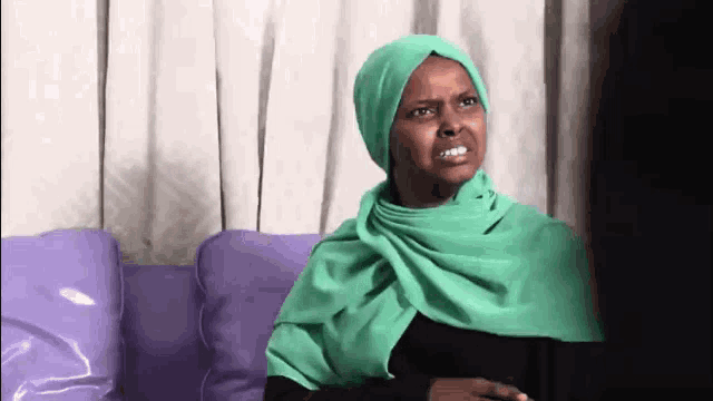 a woman wearing a green scarf is sitting on a couch making a funny face .