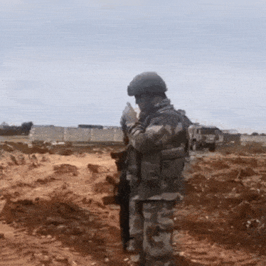 a soldier is standing in the middle of a dirt field with a gun .