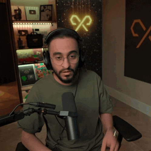 a man wearing headphones and glasses is sitting in front of a microphone in front of a neon sign that says %