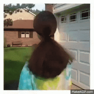 a girl with her hair in a ponytail is walking in front of a garage door