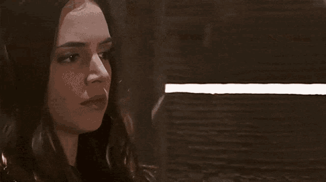 a woman in a black jacket is sitting in a dark room