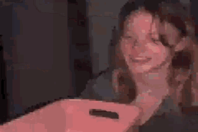 a girl is smiling while holding a pink box in her hand .
